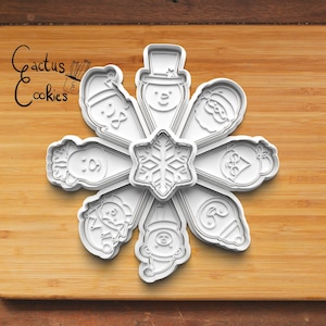 May include: A set of nine white plastic cookie cutters in the shape of a snowflake and eight different Christmas characters. The cutters are arranged in a circle on a wooden surface.