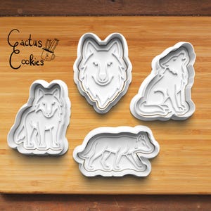 Puede incluir: Cuatro cortadores de galletas de plástico blanco con forma de lobos. Una cabeza de lobo, un lobo aullando, un lobo de pie y un lobo caminando. El texto "Cactus Cookies" está en la esquina superior izquierda.