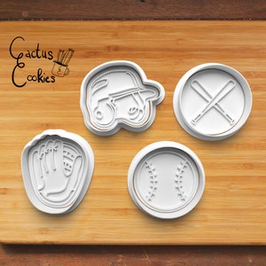 May include: Four white plastic cookie cutters shaped like a baseball, a baseball glove, a baseball bat and a baseball cap. The cutters are on a wooden surface.