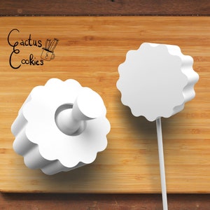 May include: Two white, flower-shaped cookie cutters on a wooden surface. One cutter has a handle, and the other is on a stick. The text "Cactus Cookies" is in the upper left corner.