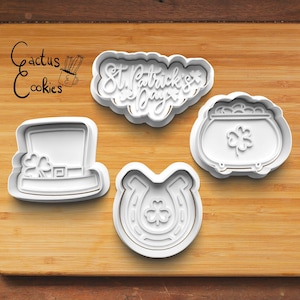 May include: Four white plastic cookie cutters shaped like a leprechaun hat, a pot of gold, a horseshoe, and the words "St. Patrick's Day".