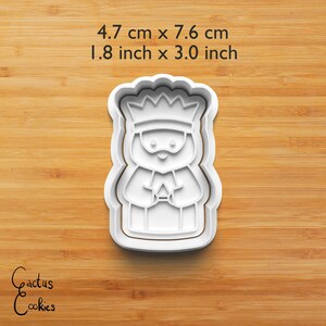 Puede incluir: Cortador de galletas de pl&aacute;stico blanco con forma de rey, de 4,7 cm por 7,6 cm (1,8 pulgadas por 3,0 pulgadas). El rey lleva una corona y sostiene un regalo. El texto "4.7 cm x 7.6 cm" y "1.8 inch x 3.0 inch" est&aacute; encima. Las palabras "Cactus Cookies" est&aacute;n en la esquina inferior izquierda.