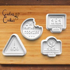 May include: Four white plastic cookie cutters on a wooden surface. The cutters are shaped like a computer screen with the text "404 Not Found", a triangle with an exclamation point and the number "404", a computer screen with a sad face and the number "404", and a bitten cookie with the text "I'm deleting cookies".
