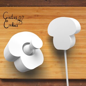 May include: Two white mushroom-shaped kitchen tools on a wooden cutting board. One is a bottle stopper, and the other is a lollipop-shaped tool. The text "Cactus Cookies" is in the upper left corner.