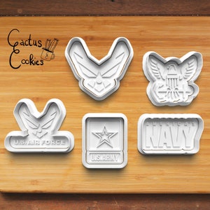 Op de afbeelding: Set van vijf witte plastic koekjesvormen met militaire logo's. De vormen omvatten de Air Force, Army, Navy en twee versies van het Air Force-logo.