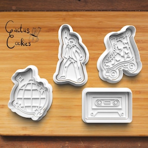 May include: Four white plastic cookie cutters in retro shapes: a disco ball, a figure in a performance pose, a roller skate with star details, and a cassette tape. The Cactus Cookies logo is in the upper left corner.