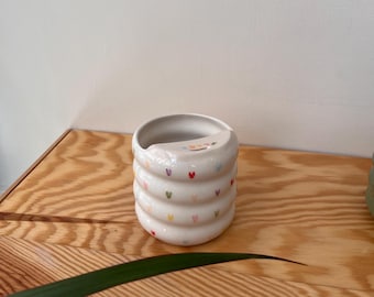 Peut inclure: Une tasse en céramique blanche avec un motif ondulé et des motifs de cœurs colorés.