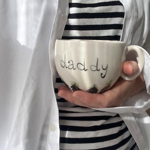 Könnte beinhalten: Weiße Keramiktasse mit dem Wort "Papa" in schwarzer Schrift.