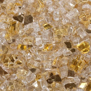 May include: A close-up of a mixture of clear and gold glass fire pit stones. The stones are small and irregular in shape, and they are scattered randomly.
