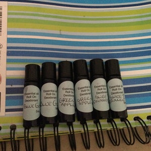 May include: Seven small glass bottles with roll-on applicators. Each bottle has a label with the text "Essential oil Roll On Deodorant" and a scent name: "Blue God", "Blue God", "Green Apple", "Green Apple", "Sweet Orange", "Sweet Orange".