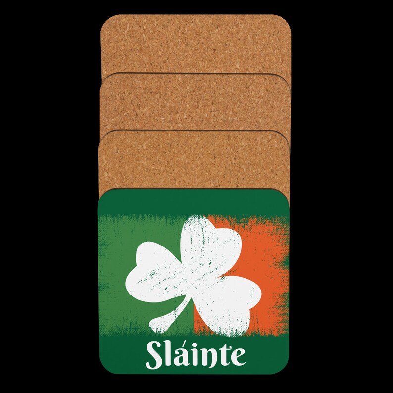 Puede incluir: Juego de cuatro posavasos de corcho con un tr&eacute;bol verde sobre un fondo naranja y blanco. Los posavasos tienen la palabra "Sl&aacute;inte" impresa en la parte inferior.