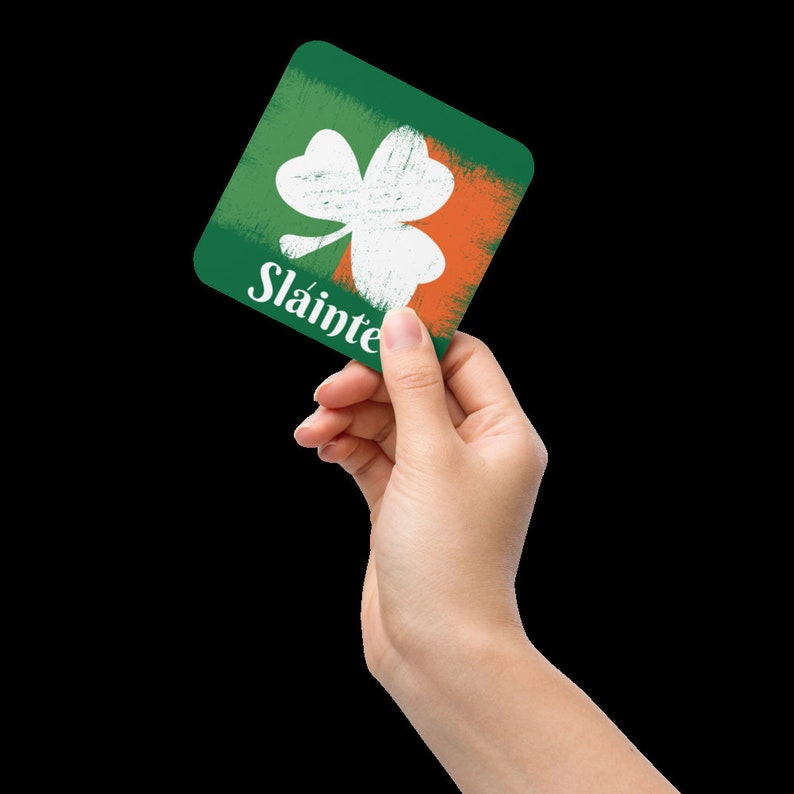 Puede incluir: Un posavasos cuadrado verde y naranja con un tr&eacute;bol blanco y la palabra "Slainte" impresa en &eacute;l.