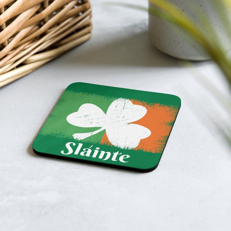 Puede incluir: Un posavasos cuadrado verde y naranja con un tr&eacute;bol blanco y la palabra "Sl&aacute;inte" en letras blancas.