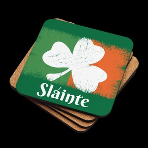 Puede incluir: Juego de cuatro posavasos verdes y naranjas con un tr&eacute;bol blanco y la palabra "Sl&aacute;inte" en letras blancas.