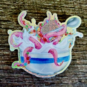 May include: A sticker of a pink octopus with colorful cereal in a white bowl with blue stripes. The octopus is surrounded by milk and a spoon is sticking out of the bowl.