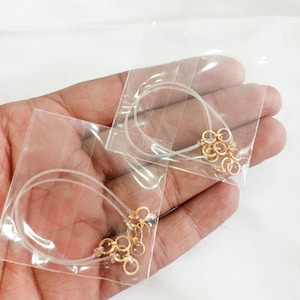 Puede incluir: Dos bolsas de plástico transparentes que contienen cordón elástico transparente con anillos de salto dorados.