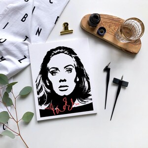Puede incluir: Retrato en blanco y negro de Adele con su nombre escrito en cursiva roja debajo. La imagen está sobre un fondo blanco.