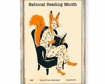 May include: A framed print titled National Reading Month featuring an orange squirrel in spotted pajamas sitting in a black armchair reading a book. The bottom text reads 1999 Stone & Press Lithography Charlotte NC. The frame is distressed light blue.