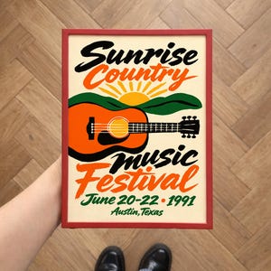 Peut inclure: Affiche encadrée avec un bord rouge, présentant une illustration de guitare et le texte du "Sunrise Country Music Festival" à Austin, Texas, du 20 au 22 juin 1991. Le design comprend un lever de soleil, des montagnes et le nom du festival.