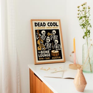 K&ouml;nnte beinhalten: Ein gerahmtes Poster mit dem Text "DEAD COOL" und "A SKELETON SWING NIGHT". Das Poster zeigt Skelettmusiker, die Instrumente spielen. Der Text "THE BONE LOUNGE" und "9PM-1AM AUSTIN" sind ebenfalls sichtbar. Der Rahmen ist holzfarben.
