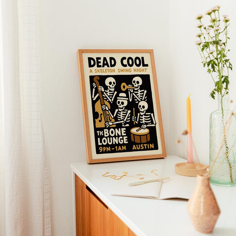 K&ouml;nnte beinhalten: Ein gerahmtes Poster mit dem Text "DEAD COOL" und "A SKELETON SWING NIGHT". Das Poster zeigt Skelettmusiker, die Instrumente spielen. Der Text "THE BONE LOUNGE" und "9PM-1AM AUSTIN" sind ebenfalls sichtbar. Der Rahmen ist holzfarben.