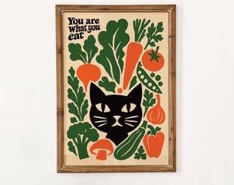 May include: A framed wall art print featuring a black cat illustration surrounded by various vegetables in orange and green colors. The text "You are what you eat" is printed in the upper left corner against a light beige background.