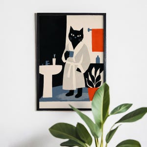 Puede incluir: Una impresi&oacute;n art&iacute;stica enmarcada representa un gato negro con una bata blanca sosteniendo una taza azul en un ba&ntilde;o. El ba&ntilde;o tiene un lavabo blanco, una toalla naranja y una planta en maceta. El fondo est&aacute; dividido en secciones negras y crema.