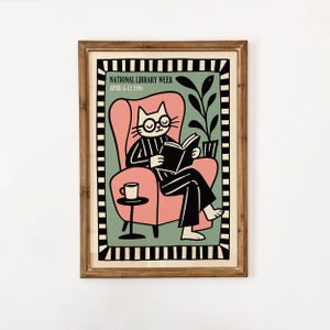 May include: A framed illustration featuring a cat wearing glasses and reading a book in a pink armchair. The image includes the text "NATIONAL LIBRARY WEEK APRIL 6-12 1998". A small table with a coffee cup is next to the chair.