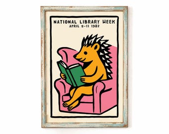 May include: A framed poster featuring a yellow hedgehog sitting in a pink armchair and reading a green book. The text at the top reads NATIONAL LIBRARY WEEK APRIL 5-11 1982. The illustration uses bold black outlines on a cream background.