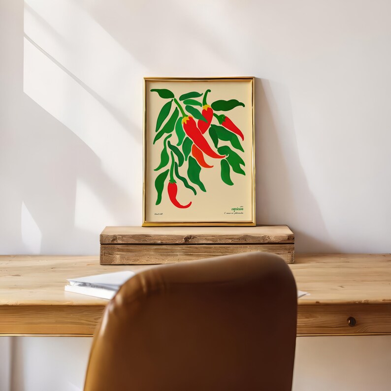 Op de afbeelding: Een ingelijste print van een botanische illustratie met een tros rode pepers met groene bladeren op een cr&egrave;mekleurige achtergrond. De tekst "Capsicum" en "Ik was zo anders" staat onder de illustratie.