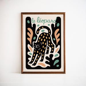 May include: A framed art print featuring a black cat with yellow spots, stretching. The cat is set against a black background with abstract shapes in peach, teal, and white. The words "le léopard" are written in teal above the cat.