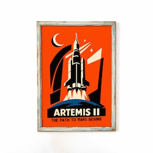 May include: A framed print with a retro space travel theme. The artwork features a rocket launching against an orange background with a crescent moon and stars. The text reads "ARTEMIS II THE PATH TO MARS BEGINS."