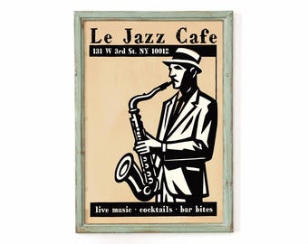 May include: A framed poster featuring a black and white illustration of a person playing a saxophone. The text reads Le Jazz Cafe, 131 W 3rd St. NY 10012, and live music cocktails bar bites. The poster is set in a light blue distressed wooden frame.