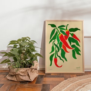 Op de afbeelding: Een ingelijste print van een gestileerde illustratie van rode pepers met groene bladeren. De print is getiteld "Capsicum" en heeft de tekst "C. annuum var. glabriusculum".