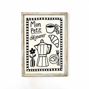 May include: A framed print with a light blue and white distressed wooden frame. The print features black and white illustrations of breakfast items, including a coffee pot, croissant, and the text "Mon Petit déjeuner".