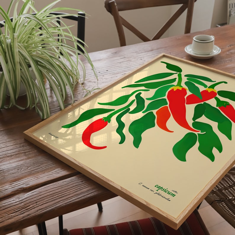 Op de afbeelding: Een ingelijste botanische illustratie van rode pepers met groene bladeren op een cr&egrave;mekleurige achtergrond. De tekst "Capsicum" en "C. annuum var. glabriusculum" is onder de illustratie gedrukt.