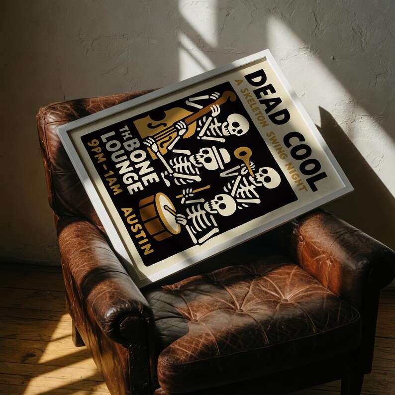 K&ouml;nnte beinhalten: Ein gerahmtes Poster mit dem Text "DEAD COOL A SKELETON SWING NIGHT" mit Skelettmusikern. Das Poster hat einen schwarzen Hintergrund mit goldenen und wei&szlig;en Akzenten. Das Poster liegt auf einem braunen Ledersessel.