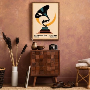 May include: A vintage-style poster with a graphic of a gramophone in a yellow and blue color scheme. The poster reads "Weekend with Jazz in Chicago" and "July 11-12, 1987 Millennium Park". The poster is framed and hanging on a wall with a brown textured surface. A wooden cabinet with a square design is in the foreground.