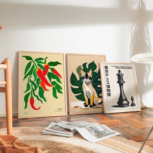 Op de afbeelding: Drie ingelijste prints met verschillende ontwerpen. De eerste print toont een groene, bladerrijke tak met rode pepers op een cr&egrave;me achtergrond. De tweede print toont een zwart-witte kat die op een groen blad zit op een cr&egrave;me achtergrond. De derde print toont een zwart schaakstuk op een witte achtergrond met de tekst "Tokyo Chess Museum" in het Japans en Engels.