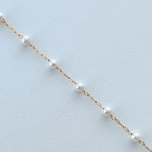 May include: A delicate gold chain necklace with small white pearls spaced evenly along the chain.