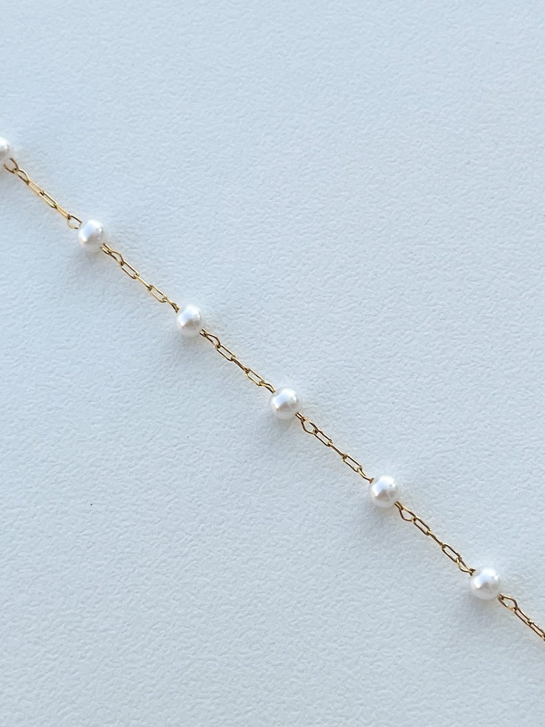 May include: A delicate gold chain necklace with small white pearls spaced evenly along the chain.