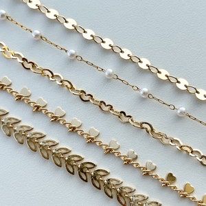 May include: Five gold chains with different styles, including a chain with small round links, a chain with small heart charms, a chain with small leaf charms, and a chain with small pearl accents.