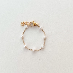 May include: A delicate gold chain bracelet with small white pearls.