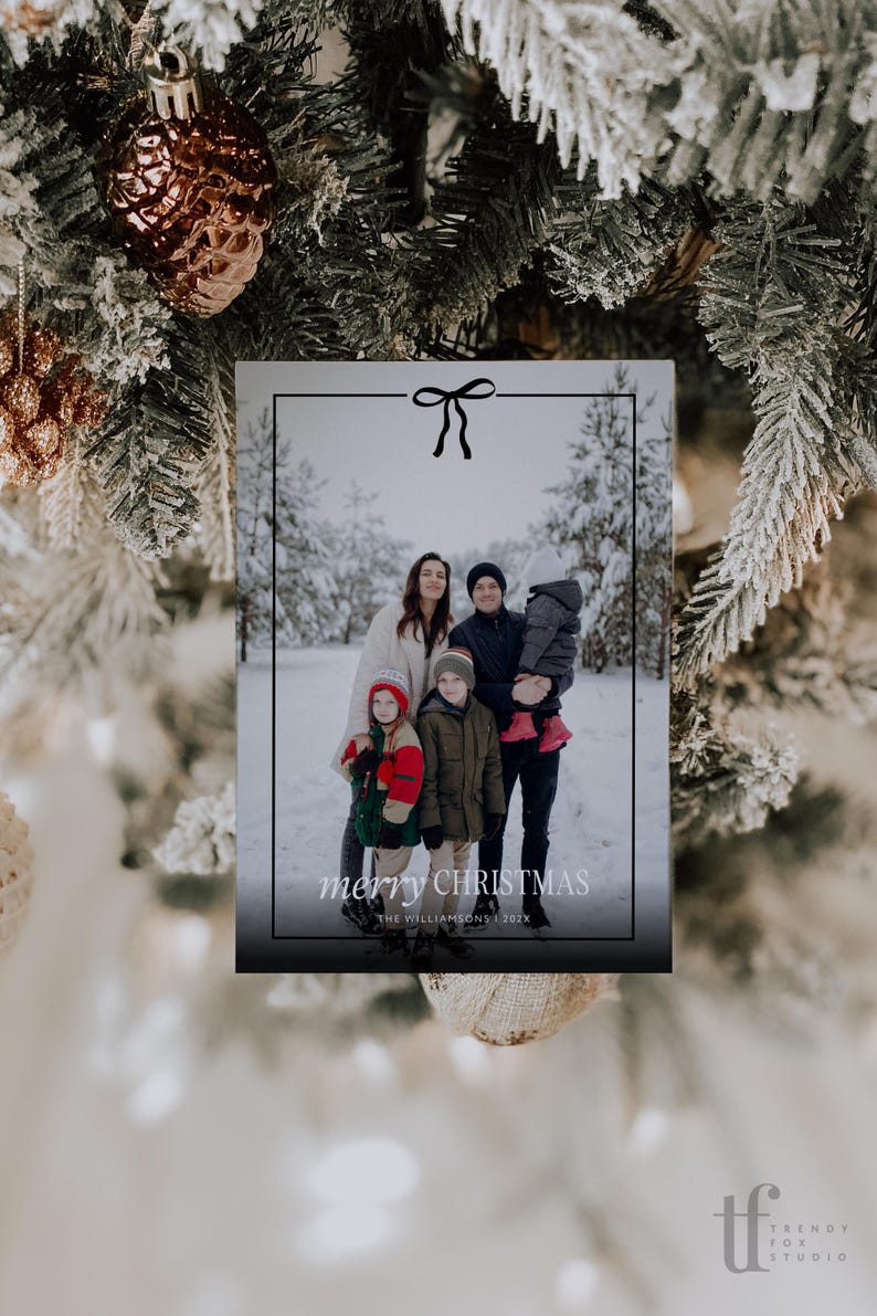 Pode incluir: Cart&atilde;o de Natal com uma foto de fam&iacute;lia numa floresta nevada. O cart&atilde;o tem uma borda preta com um la&ccedil;o e a inscri&ccedil;&atilde;o "merry CHRISTMAS". A fam&iacute;lia est&aacute; vestida com roupas de inverno.