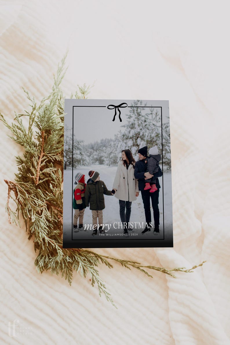 Pode incluir: Um cart&atilde;o de Natal com uma foto de fam&iacute;lia numa floresta nevada. O cart&atilde;o tem uma borda preta com um la&ccedil;o e as palavras "merry CHRISTMAS" em branco. A fam&iacute;lia est&aacute; vestida com roupas de inverno.