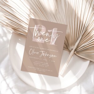 May include: A beige invitation card with the text "Twenty one" in white script with a pink background. The text "Join us as we celebrate the birthday of Olivia Johnson" is printed below the number. The date and time of the event are listed below the name.