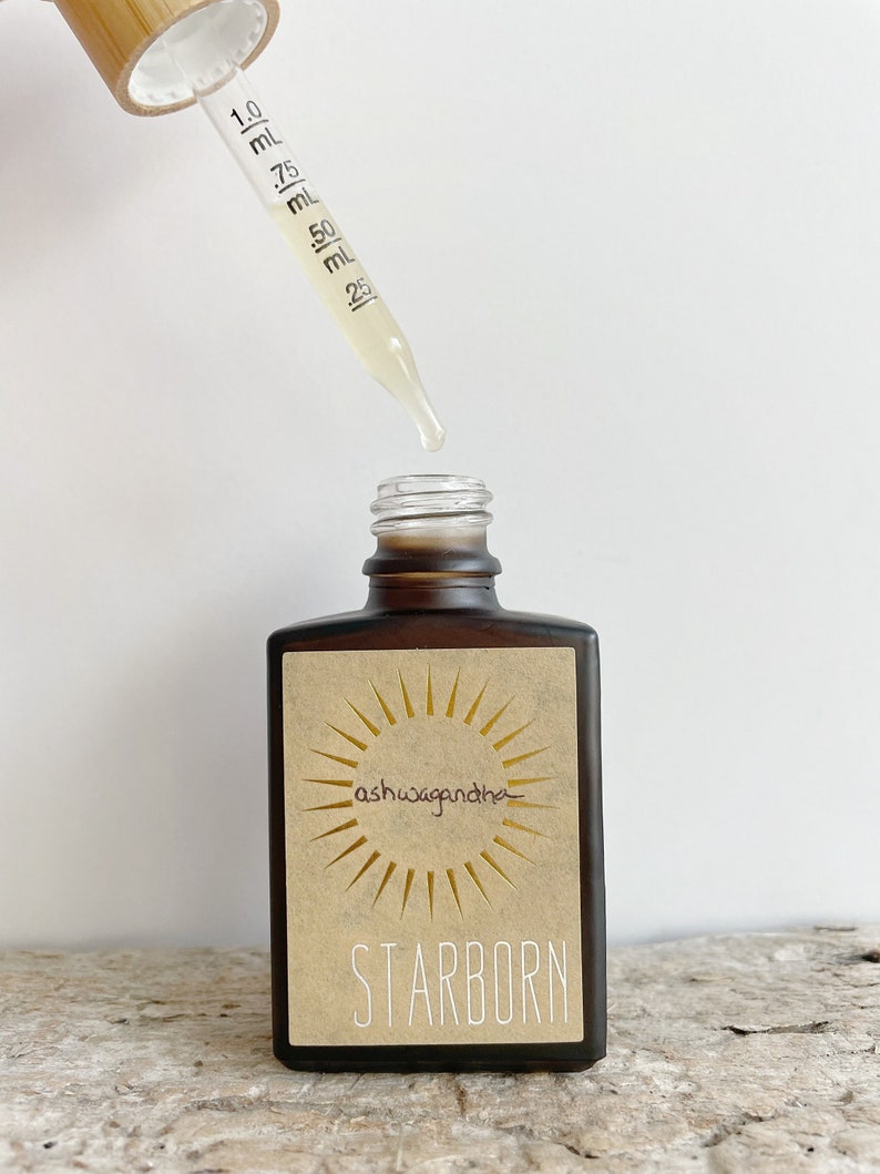 K&ouml;nnte beinhalten: Eine braune Glasflasche mit einer Pipette, gef&uuml;llt mit einer hellgelben Fl&uuml;ssigkeit. Die Flasche hat ein Etikett mit einer Sonnengrafik und dem Text "ashwagandha" und "STARBORN".