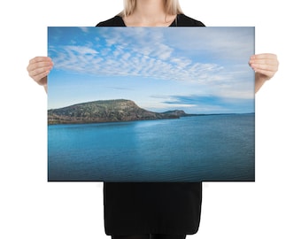 May include: A panoramic view of a lake with a wooded island in the distance. The sky is a bright blue with wispy white clouds.
