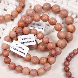 Op de afbeelding: Verschillende armbanden gemaakt van lichtbruine houten kralen. Elke armband bestaat uit ronde kralen met zichtbare houtnerf. De armbanden zijn voorzien van labels met de tekst "Crystal Department".