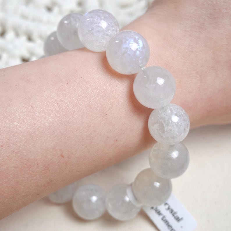 May include: White crystal bead bracelet with iridescent shimmer. The bracelet is made of round, smooth beads and is worn on a person's wrist.